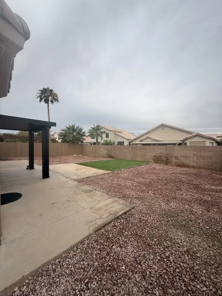 Backyard with turf, red rock and a concrete patio, seen from the house